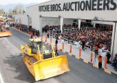 A crawler tractor crosses the ramp in front of a crowd of seated bidders in the auction theater in Chilliwack, B.C. in March 2010. Most mobile equipment is driven over a ramp in front of a crowd of bidders. (Photo courtesy of Ritchie Bros. Auctioneers)