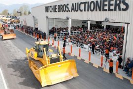 A crawler tractor crosses the ramp in front of a crowd of seated bidders in the auction theater in Chilliwack, B.C. in March 2010. Most mobile equipment is driven over a ramp in front of a crowd of bidders. (Photo courtesy of Ritchie Bros. Auctioneers)