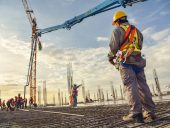 A construction worker control a pouring concrete pump on construction site and sunset background