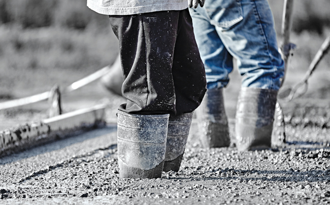 Concrete workers in heavy boots working in new wet concrete.